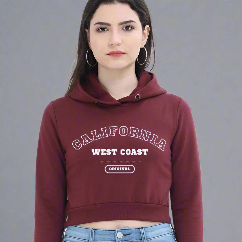 A woman wearing a red California crop hoodie with 'CALIFORNIA' and 'WEST COAST' text on the front and 'ORIGINALS' on the sleeve, paired with blue jeans.
